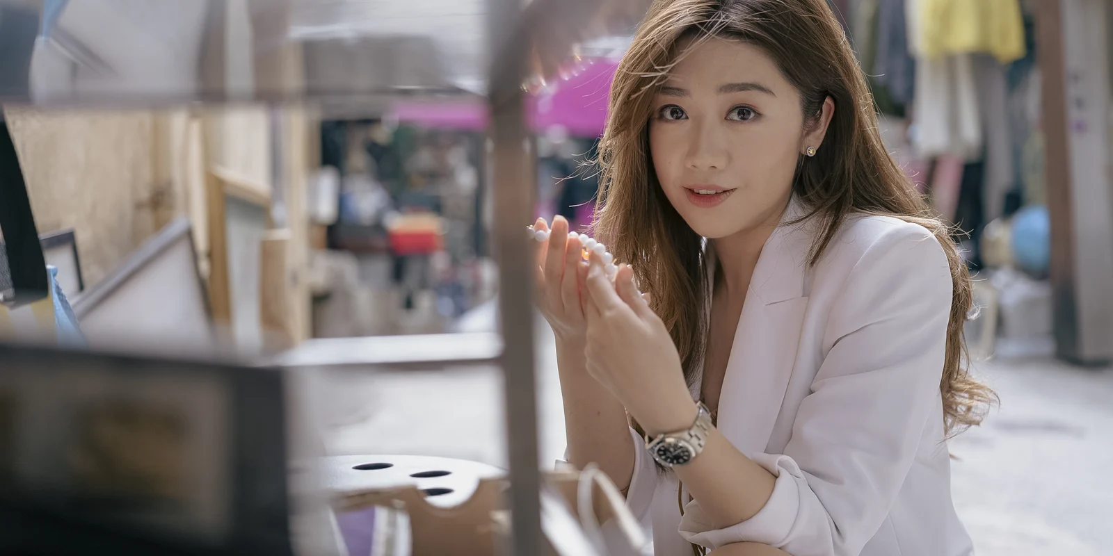 Ivy Liu in a pale suit gestures toward the camera in a softly layered Hong Kong street scene