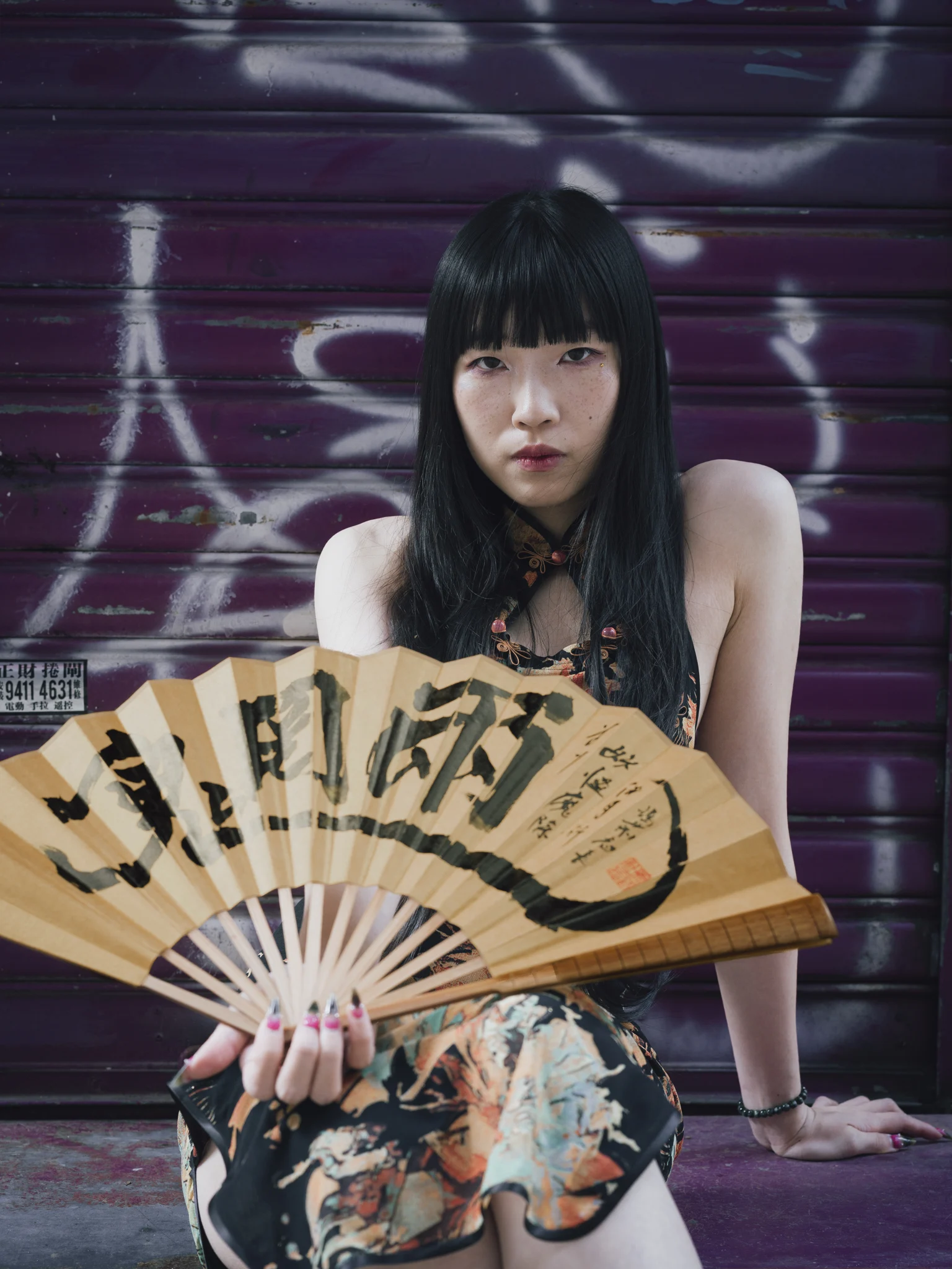 Merry Cheung holds a painted calligraphy fan toward the camera before a purple Hong Kong shutter