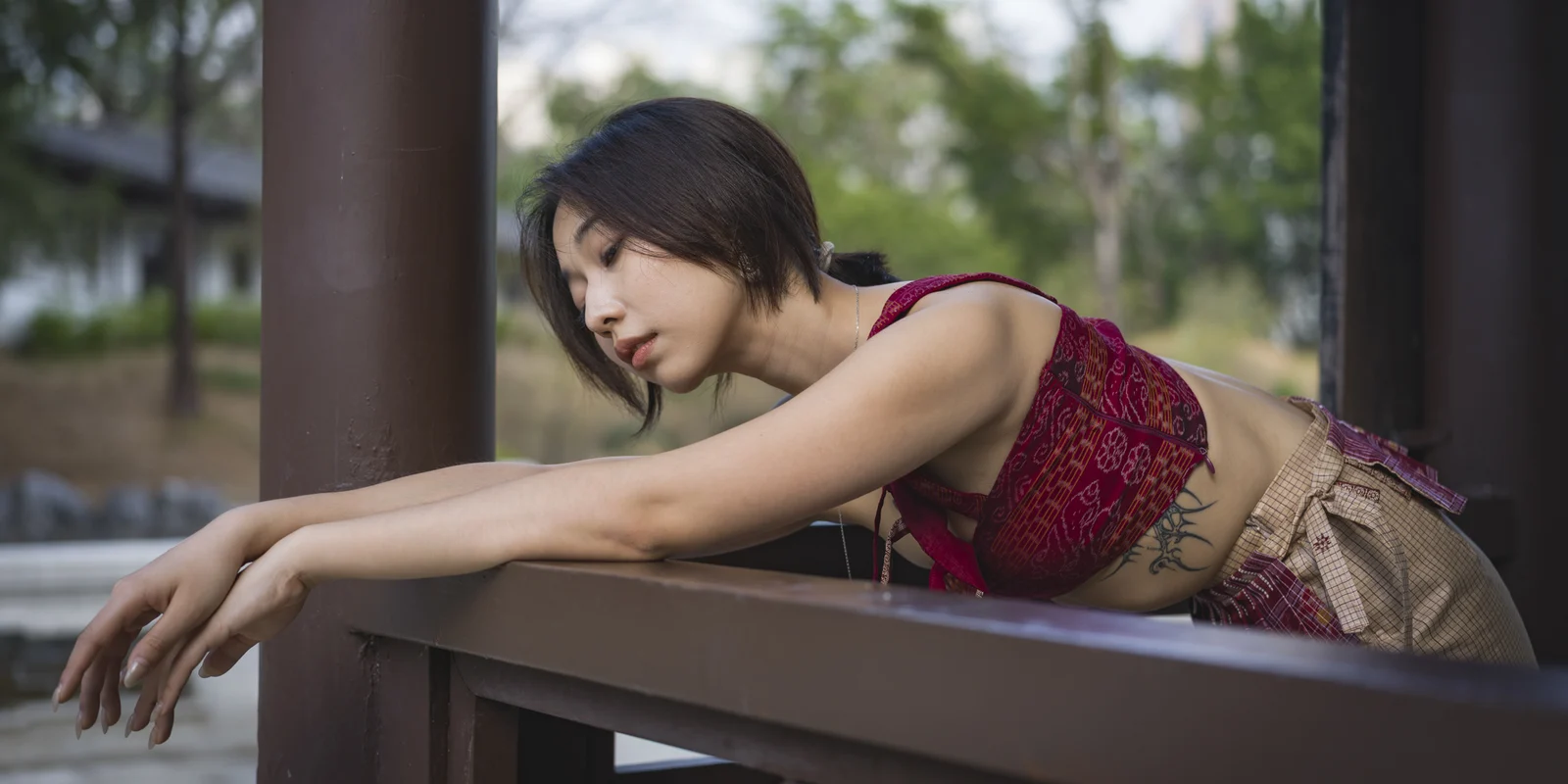 Chow leans across a wooden garden rail wearing a red and gold Sarangi design