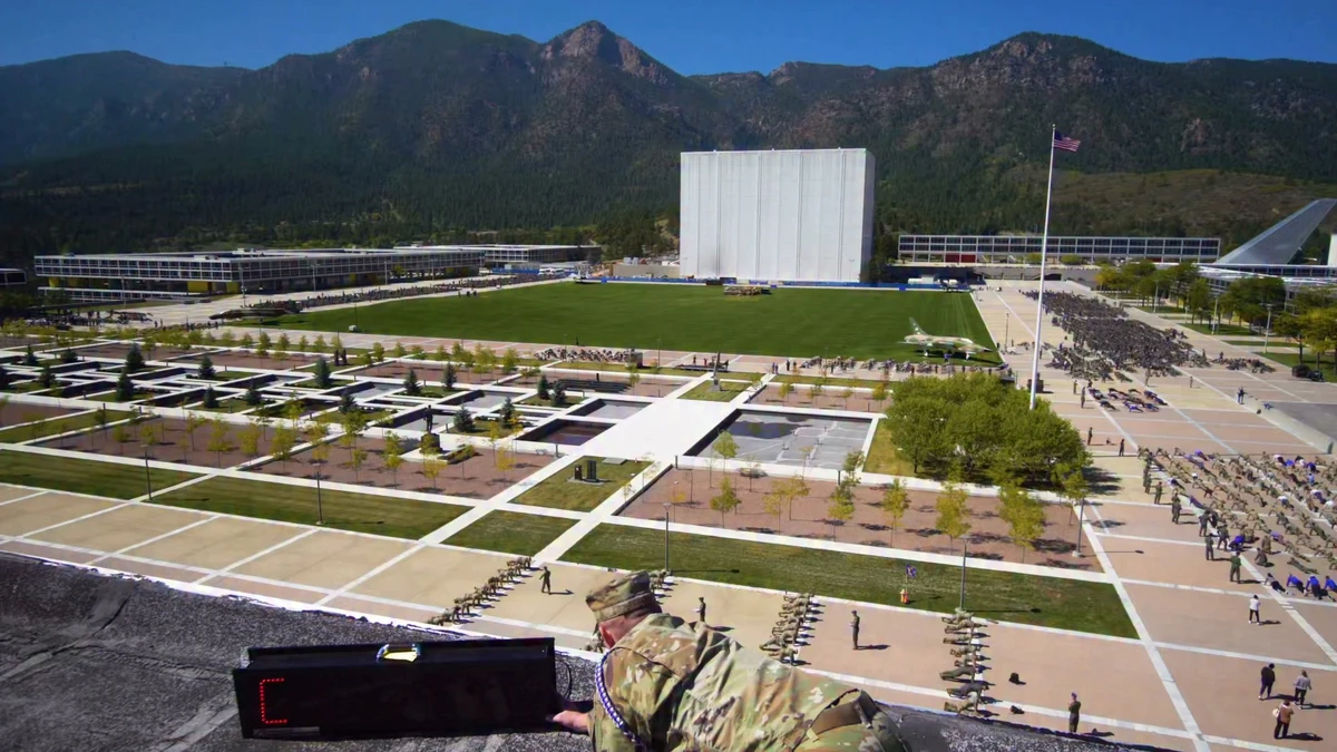 An elevated documentary video still from the October 2 Air Force Academy push-up event shows long rows of participants around the campus lawn with mountains behind them