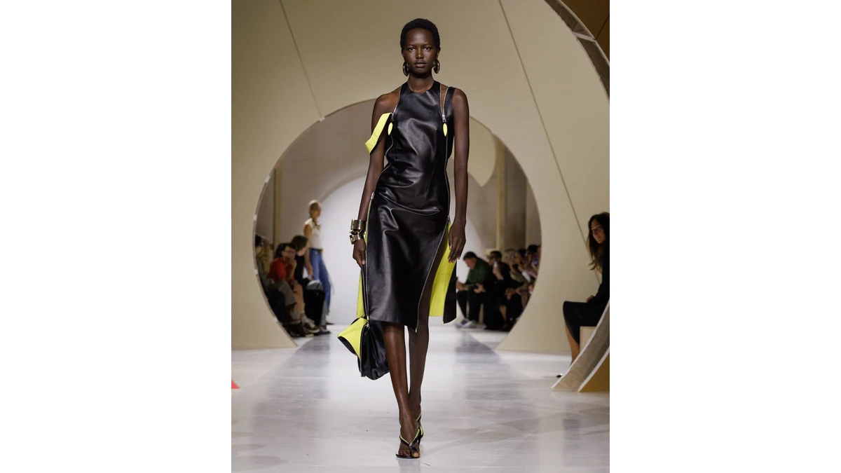 Givenchy Spring/Summer 2027 opening look, a black leather dress with yellow visible at the sides and hem, photographed on the runway.
