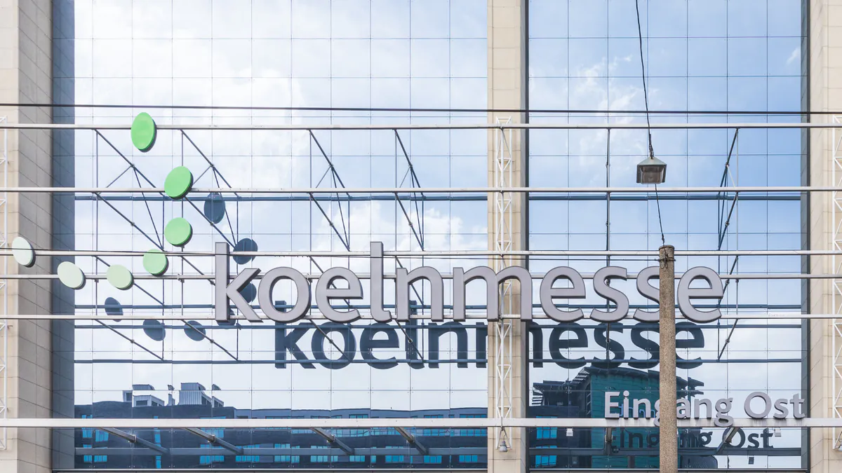 Raimond Spekking’s 2018 photograph shows the glass east entrance of Koelnmesse in Cologne, with the venue’s metallic name above the facade