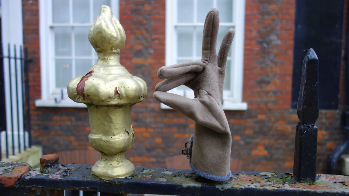 A grey glove appears to make a hand gesture beside a gold-painted railing finial on Bedford Row in London.