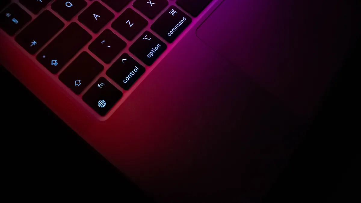 Close-up photograph of a 2020 M1 MacBook Pro keyboard and trackpad under purple light.