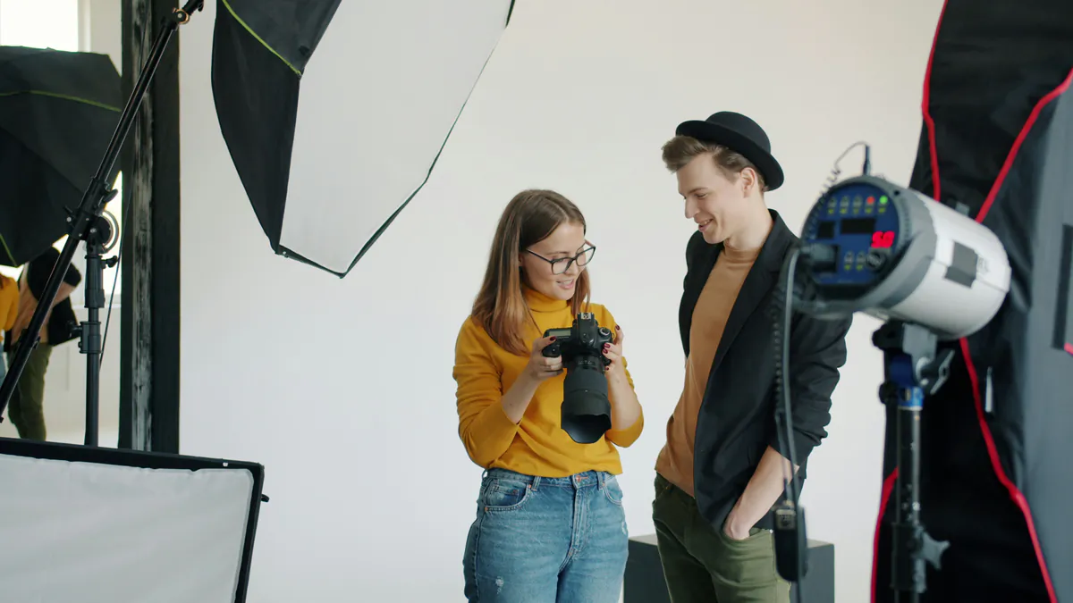 Photographer and subject reviewing a camera image amid studio softboxes, flash units and a reflector.