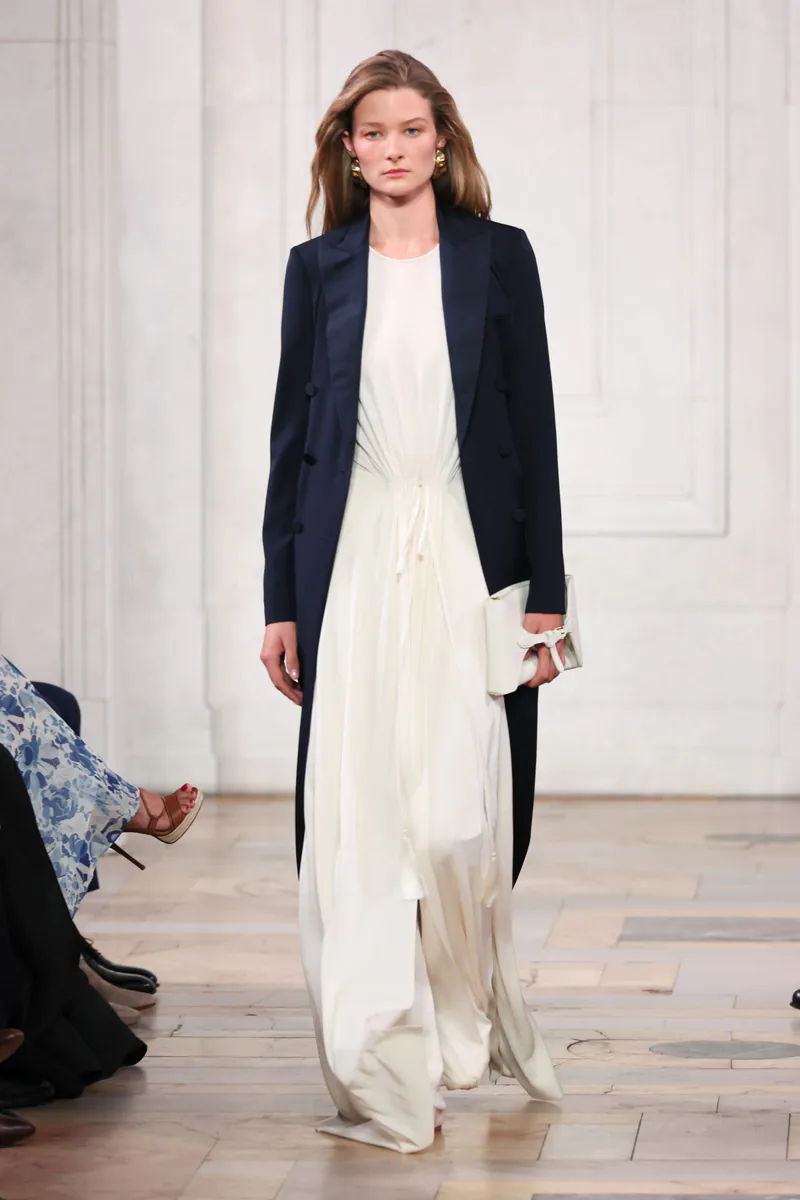 Model in a fluid white dress under a navy tailored coat at Ralph Lauren Spring 2027.