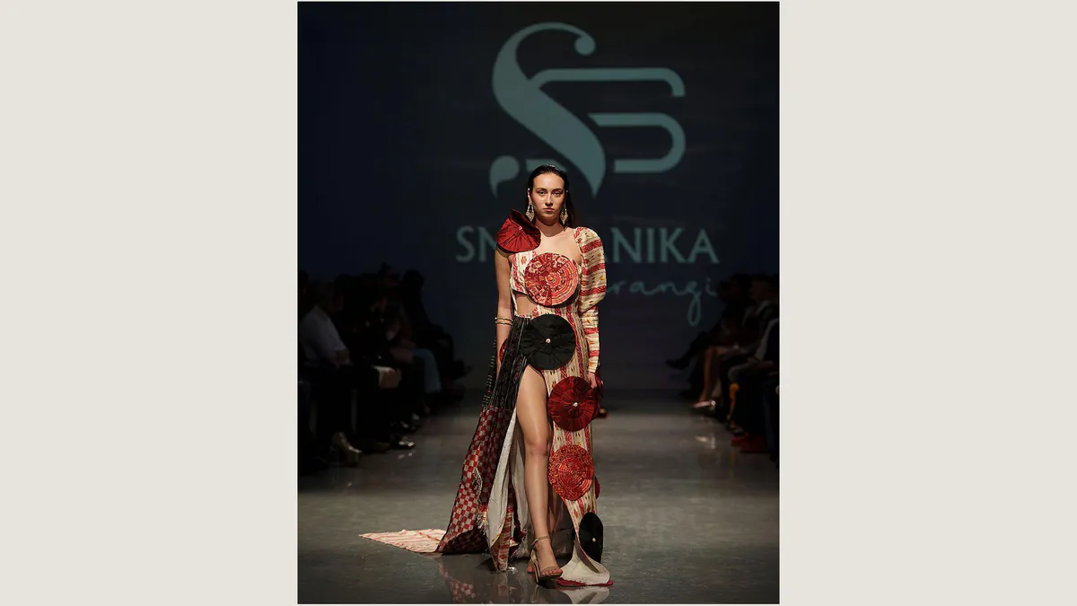 A model wears a cream, red, and black Smaranika Sarangi design with circular fabric details on the Asian NYFW runway.