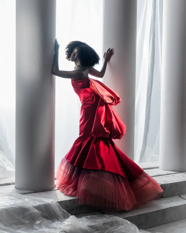 Fashion editorial model in a red gown framed by tall white columns