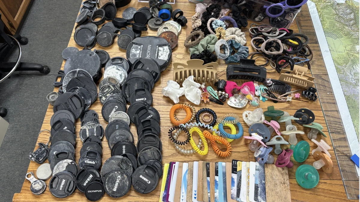 Recovered camera lens caps, hair accessories, sunglasses, keys, and pacifiers arranged on a table by Yellowstone staff.